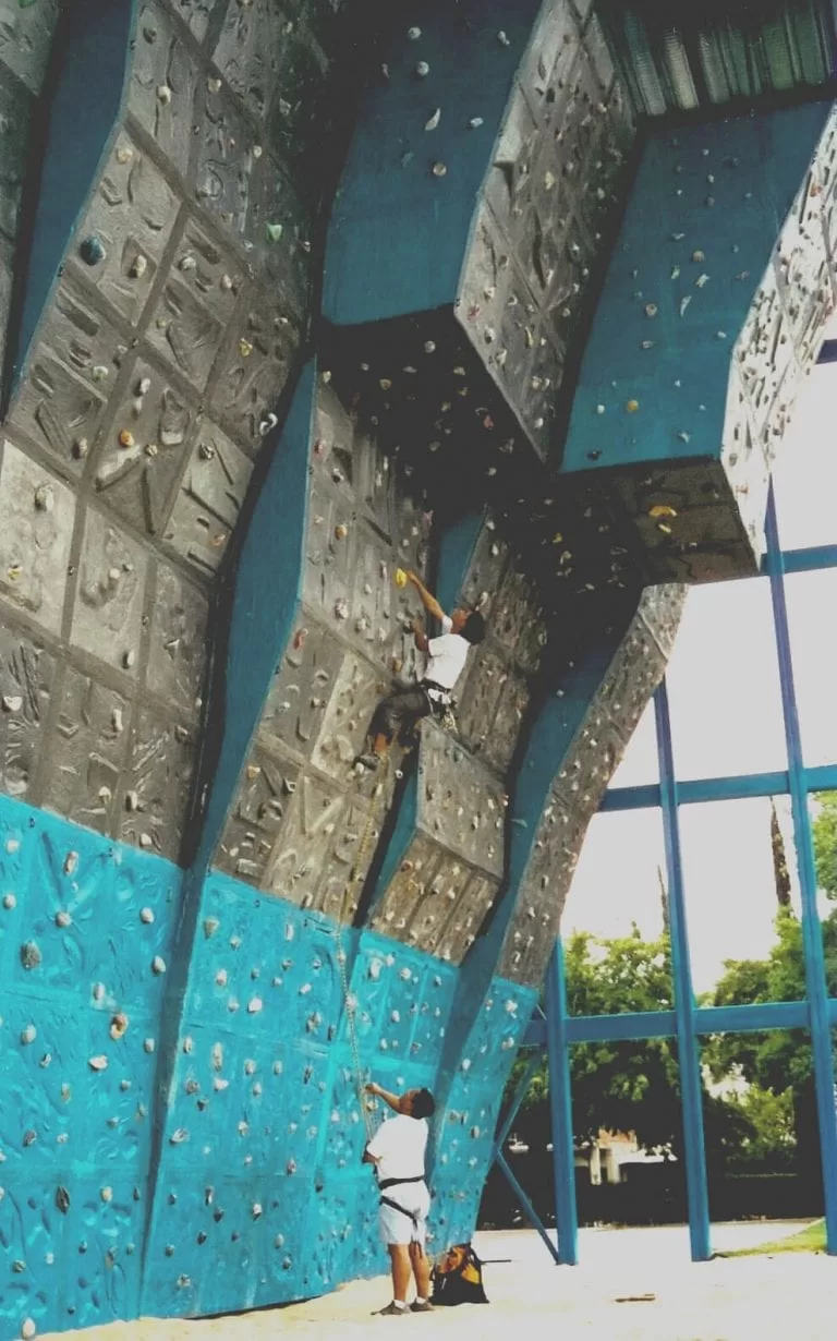 Ecoproparks. Una persona disfrutando de la emocionante escalada en una pared llena de rocas en Ecoproparks, mientras otra brinda asesoramiento para garantizar la seguridad en la aventura.